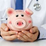 Male medicine doctor wearing blue tie holding and covering happy funny smiling piggybank in hands  